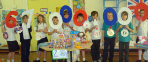 Children holding up giant numbers, showing 67,000,000, with 'gold medal' artwork around their necks