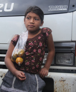 Young girl with bag of fruit, standing in front of a bus