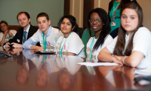 Young people in Send My Friend to School t shirts, seated at a table, listening intently