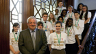 Man in suit with group of young people in Send My Friend to School tshjrts, standing on a staircase