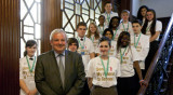 Man in suit with group of young people in Send My Friend to School tshjrts, standing on a staircase