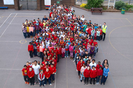 Children standing in a playground arranged to form the figure of a girl.