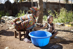 Girl washing younger child with water from a bucket