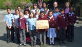 Group of children and adults in playground, holding up large envelope