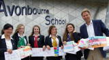 Man and schoolgirls with scarf artwork in front of a sign reading 'Avonbourne School'