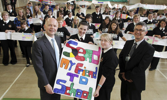 Children and adults display Send My Friend to School banner, with more children displaying a paper scarf