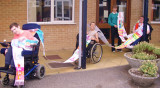 Children in wheelchairs holding a long paper scarf with artwork.