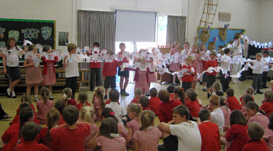 School Assembly, with children holding up paper 'sister' figures.