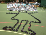 Shoes laid out to form the shape of a girl on a playground, with group of children in the background,