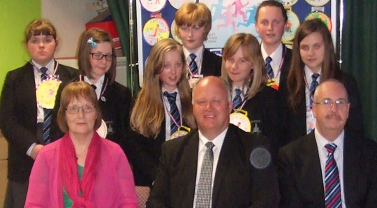 School students and adults with a display of gold medal artwork.