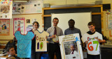 Two pupils with MP and teacher in school classroom, displaying sport jersey artwork.