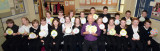 Large group of teenagers in a classroom, with teacher, holding up gold medal artwork.