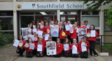 Large group of children in uniform with posters and artwork, outside a school building.