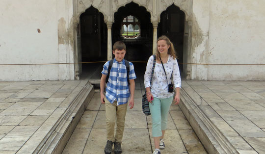 Boy and girl walking towards the camera, in front of an Indian building.