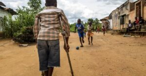 A child, Zambo, who has a physical impairment, watches his friends play at a Sightsavers supported inclusive school in Cameroon. Copyright: Sightsavers/Rodrig Mbok.